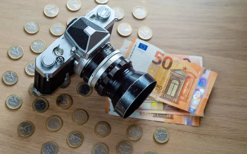 uro banknotes, coins and a camera on a light wooden background.